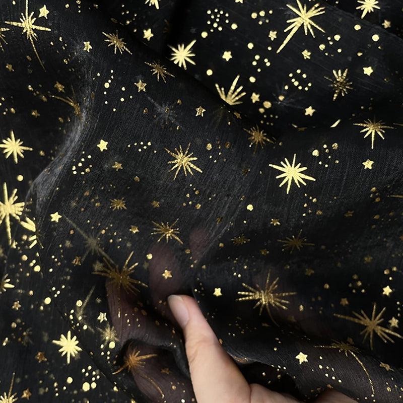 Une main présente le Tissu organza étoilé au mètre de Longan Craft France, un tissu organza noir transparent orné d'étoiles et d'éclats d'or, parfait pour les robes de mariée et les costumes.