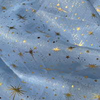 Le Tissu organza étoilé au mètre de Longan Craft France présente un imprimé bleu clair décoré d'étoiles dorées, idéal pour la création de robes et costumes de mariage grâce à sa matière légère et ses multiples applications créatives.