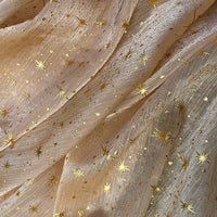 Tissu organza étoilé au mètre de Longan Craft France : organza beige clair imprimé de motifs étoiles et points dorés, légèrement texturé, translucide et souple, idéal pour robes de mariée et costumes de mariage.
