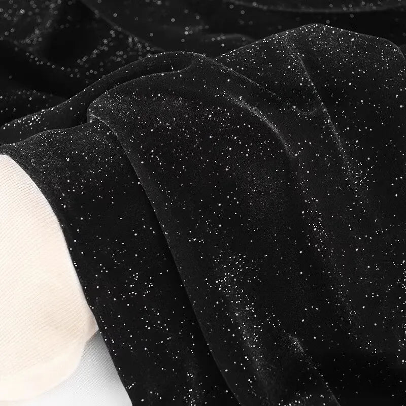 Gros plan sur le tissu velours pailleté au mètre de Longan Craft France : velours polyester doux argenté avec une finition étincelante, drapé en plis souples. Un bord blanc apparaît dans le coin - idéal pour la décoration, les robes de soirée et la couture DIY.