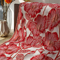 Le Tissu brocart floral 3D en fil d'or de Longan Craft France, orné de coquelicots rouges en relief, est drapé sur une table. Des vases en verre contenant des fleurs séchées et un pichet géométrique beige complètent l'ensemble.