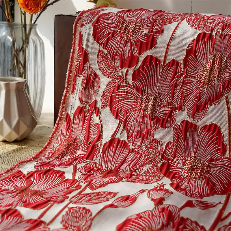 Le Tissu brocart floral 3D en fil d'or de Longan Craft France, orné de coquelicots rouges en relief, est drapé sur une table. Des vases en verre contenant des fleurs séchées et un pichet géométrique beige complètent l'ensemble.
