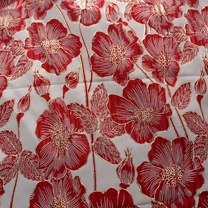 Gros plan sur le Tissu brocart floral 3D en fil d'or de Longan Craft France, un élégant tissu jacquard représentant de grandes fleurs rouges avec des contours blancs et des fils d'or sur un fond clair, avec à la fois des fleurs épanouies et des boutons fermés.