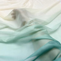 Un pied et une jambe reposent sur une surface douce, partiellement drapée de Mousseline transparente dégradée au mètre de Longan Craft France - un tissu transparent à effet dégradé, blanc et vert pâle, qui confère à la scène un aspect aérien et délicat.