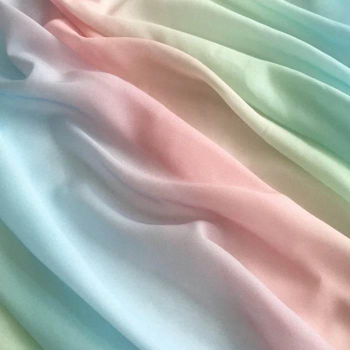 Un gros plan du Tissu en mousseline dégradé arc-en-ciel au mètre de Longan Craft France montre des teintes douces et pastel de bleu, de rose et de vert menthe qui se mélangent en douceur avec des plis délicats - idéal pour confectionner des robes, des chemisiers ou des décorations.