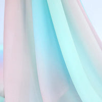 Gros plan sur le Tissu en mousseline dégradé arc-en-ciel de Longan Craft France, aux teintes pastel roses et bleues, aux plis souples et à la texture douce, idéal pour les peignoirs, les chemisiers ou les décors. Le fond flou donne une impression de légèreté.