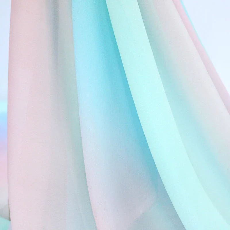 Gros plan sur le Tissu en mousseline dégradé arc-en-ciel de Longan Craft France, aux teintes pastel roses et bleues, aux plis souples et à la texture douce, idéal pour les peignoirs, les chemisiers ou les décors. Le fond flou donne une impression de légèreté.