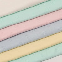 Une pile de six tissus pointelle jacquard en forme de cœur au mètre de Longan Craft France - des tissus en maille fine et douce avec des motifs de cœur subtils, idéaux pour le bricolage de vêtements d'été pour bébés et enfants.