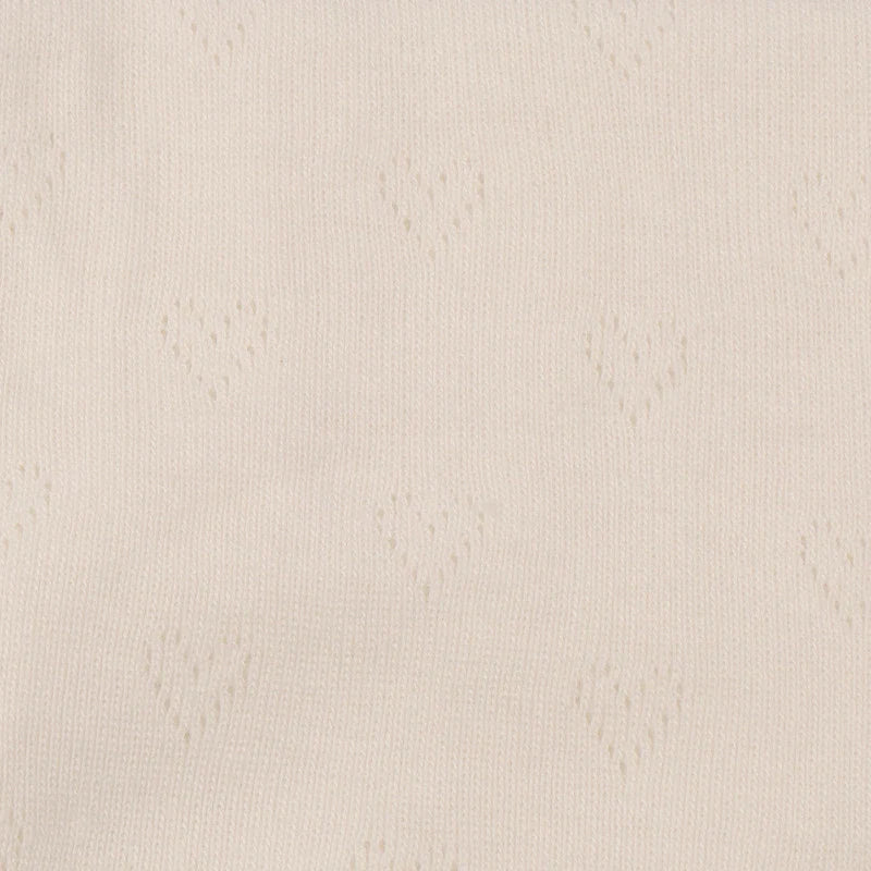 Gros plan sur le tissu pointelle jacquard en forme de cœur beige clair de Longan Craft France, un fin tricot d'été au mètre, idéal pour le bricolage de vêtements pour bébés et enfants avec ses délicats trous en forme de cœur.