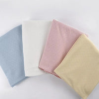 Quatre pièces de tissu pointelle cœur au mètre de Longan Craft France en bleu clair, blanc, rose et jaune sont disposées sur une surface blanche - un tissu extensible idéal pour les couches de base et les vêtements d'intérieur DIY.