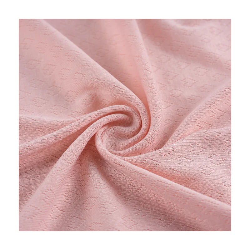 Un gros plan sur le tissu pointelle cœur au mètre de Longan Craft France montre son tissu rose pâle, doux et extensible, avec un subtil motif de losanges. Il est parfait pour les couches de base et les vêtements d'intérieur DIY.