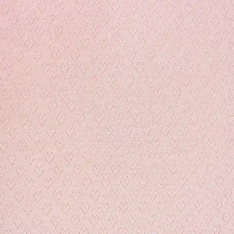 Un gros plan sur le tissu pointelle cœur au mètre de Longan Craft France révèle son tissu extensible rose pâle, uniformément texturé avec de petits cœurs gaufrés - une matière de haute qualité idéale pour les couches de base DIY ou les vêtements d'intérieur.