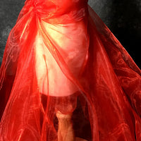 Une lampe enveloppée dans le tissu organza irisé au mètre de Longan Craft France crée une chaude lueur rouge, car la matière transparente et aérienne se drape et se noue doucement autour de l'abat-jour.