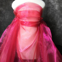 La tête d'un mannequin est drapée de Tissu organza irisé au mètre de Longan Craft France, un tissu organza rose cristal brillant, couvrant la tête et le cou sur un fond texturé sombre.