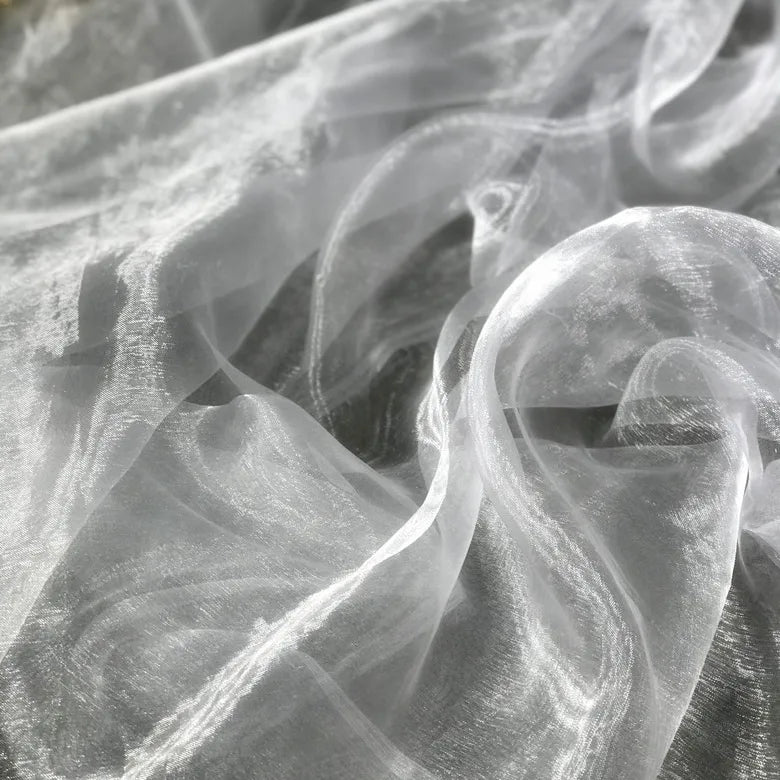 Un gros plan de Tissu organza irisé au mètre de Longan Craft France révèle son organza cristal blanc translucide aux plis doux et à la brillance subtile, idéal pour les projets de couture et de décoration élégants.