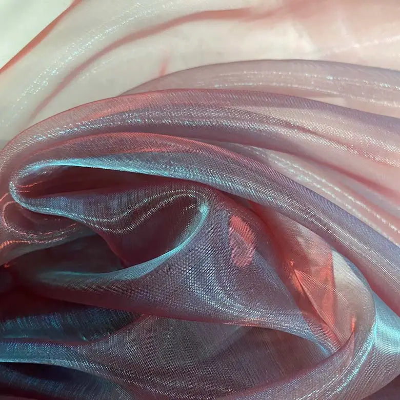 Gros plan sur Tissu organza irisé au mètre de Longan Craft France, un tissu organza cristal transparent et scintillant dans les tons bleu clair et rose, délicatement superposé avec des plis doux et des reflets délicats. Parfait pour les robes et les projets spéciaux.