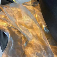 Gros plan sur Tissu organza irisé au mètre de Longan Craft France, montrant un cristal d'organza doré diaphane et irisé drapé sur du noir, la lumière se reflétant sur sa texture brillante et translucide.