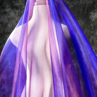 Une robe est drapée d'organza Tissu irisé au mètre de Longan Craft France, dont les reflets violets et bleus, semblables à des cristaux, créent un magnifique dégradé sur un fond texturé gris foncé.