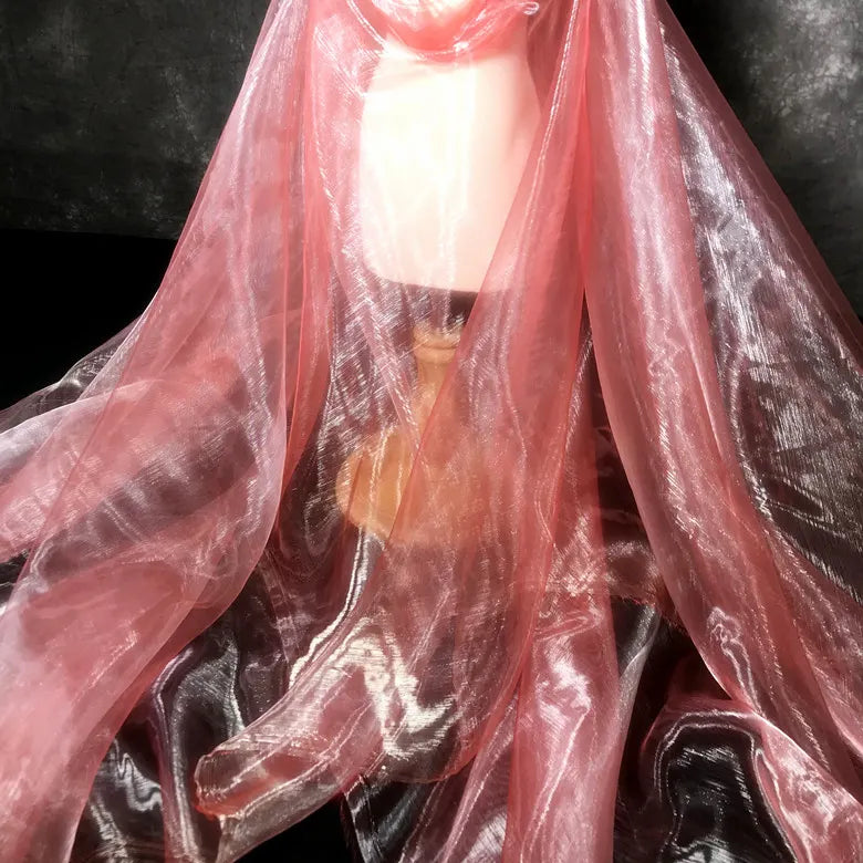Une lampe avec un abat-jour beige et une base en bois est ornée de Tissu organza irisé au mètre de Longan Craft France, un tissu organza cristal rose scintillant, présenté sur un fond sombre.