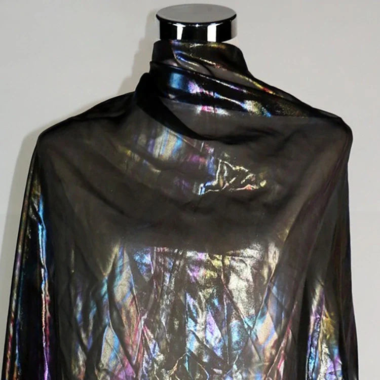 Un mannequin présente Mousseline irisée au mètre, une mousseline de polyester métallisée de Longan Craft France, qui scintille de nuances arc-en-ciel sous la lumière. Le fond reste uni et neutre, idéal pour mettre en valeur ce tissu DIY.