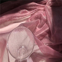 Un verre transparent est posé sur le Tissu en tulle bicolore irisé au mètre de Longan Craft France, un tissu chatoyant, semblable à une maille, dont les plis et les reflets irisés sont mis en valeur par la lumière - idéal pour créer des robes éblouissantes.