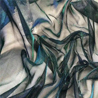 Gros plan sur Tissu en tulle bicolore irisé au mètre de Longan Craft France - une maille noire transparente aux reflets bleus et verts, superposée en plis souples - idéale comme tissu tulle scintillant pour robe.