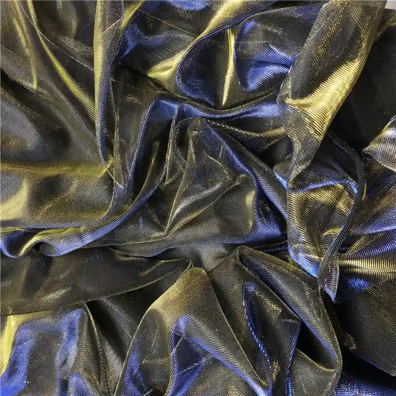 Un gros plan sur un tissu froissé, semi-transparent et métallisé noir et or montre la brillance subtile et la surface texturée du Tissu en tulle bicolore irisé au mètre de Longan Craft France - idéal pour une robe de soirée scintillante.
