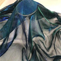 Le Tissu en tulle bicolore irisé au mètre de Longan Craft France se compose d'un tissu transparent et léger aux reflets bleus et verts, drapé pour obtenir des plis souples et un effet semi-transparent - parfait comme tulle scintillant pour les robes.