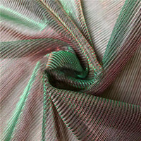 Gros plan sur le Tissu en tulle bicolore irisé au mètre de Longan Craft France, une maille vert et rose chatoyante idéale pour une robe de soirée ou un costume, montrant des plis froncés et des fils qui attirent la lumière.