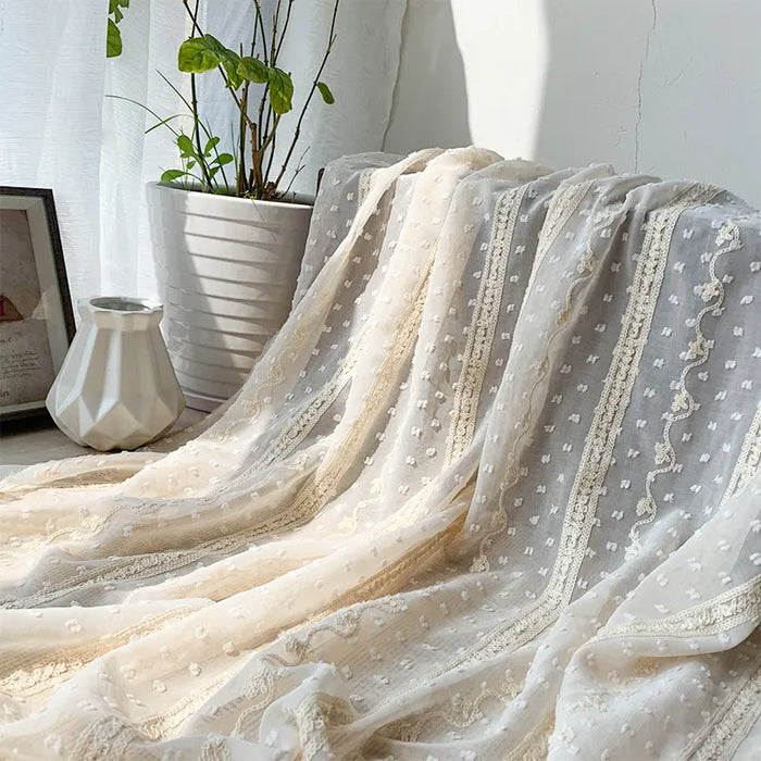 Tissu en mousseline jacquard à rayures et pois Longan Craft France drapé, créant une ambiance légère et élégante. À l'arrière-plan : pot blanc avec plante verte, cadre photo et vase céramique blanche pour la déco.