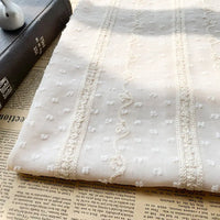 Le tissu en mousseline jacquard à rayures et pois de Longan Craft France, parfait pour vêtements ou déco légère, est présenté sur un journal ouvert et un livre fermé, apportant légèreté et élégance à votre prochain projet.