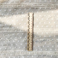 Une règle en bois est posée verticalement sur le tissu en mousseline jacquard à rayures et pois au mètre de Longan Craft France, un tissu beige avec des motifs de dentelle et de pointillés, idéal pour les vêtements aérés et les décors élégants. La règle indique des mesures en centimètres.
