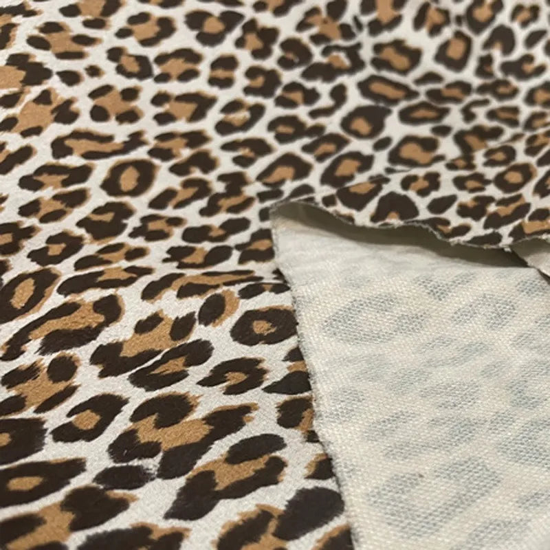 Gros plan sur la Suédine imprimée léopard au mètre de Longan Craft France, retournée pour révéler le dessous plus clair ; ses taches brunes et noires sur fond fauve en font un tissu imitation cuir suédé DIY idéal pour les chapeaux, les chaussures et les vêtements.