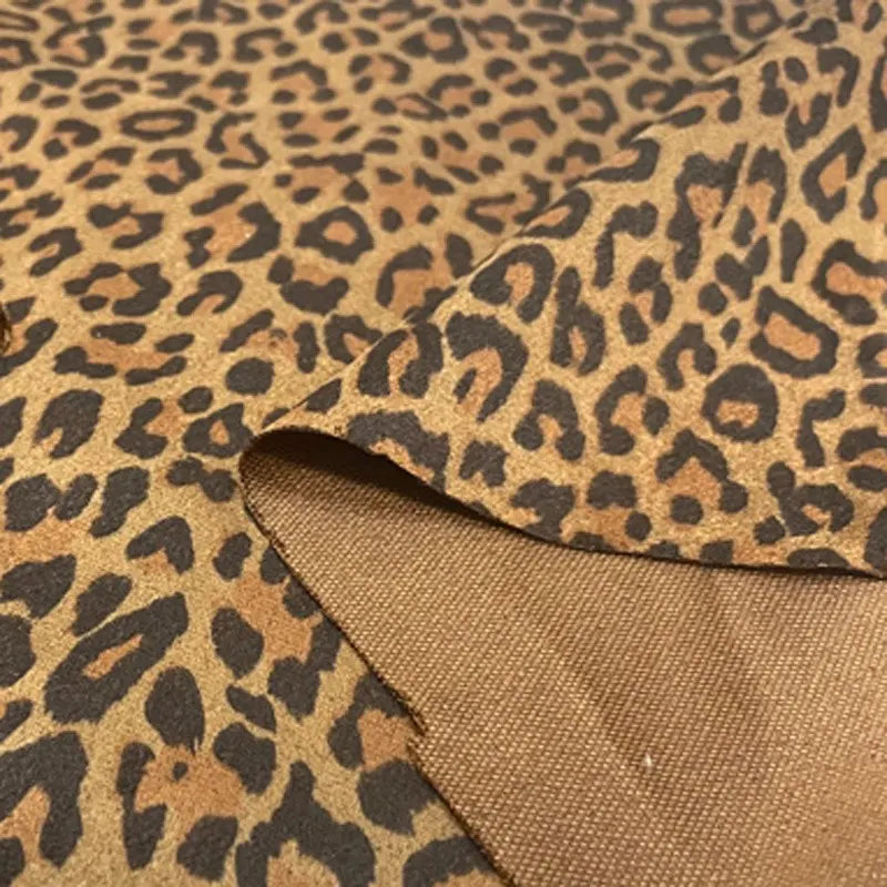 Un gros plan de la Suédine imprimée léopard au mètre par Longan Craft France montre son motif léopard brun et noir ; un coin de ce tissu imitation cuir suédé est légèrement plié, révélant le dessous brun uni.