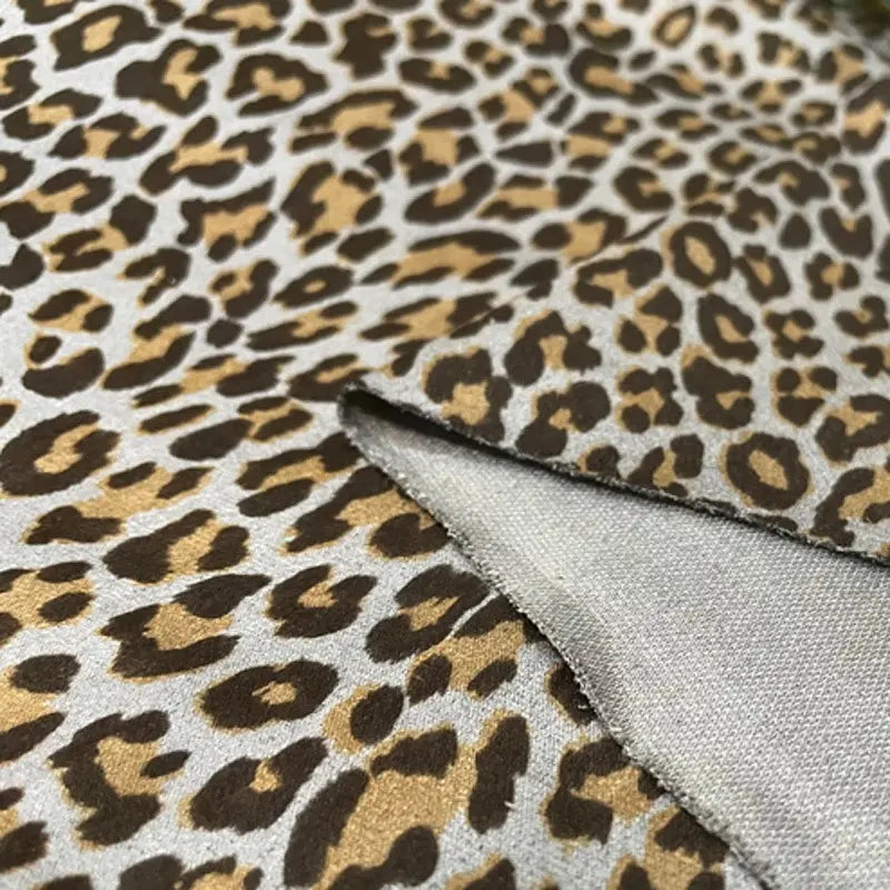 Gros plan sur deux pièces de Suédine imprimée léopard au mètre de Longan Craft France en marron, tan et noir. L'un des morceaux est plié pour montrer le dessous de ce tissu doux imitant le cuir suédé, idéal pour les chapeaux, les chaussures et les vêtements DIY.