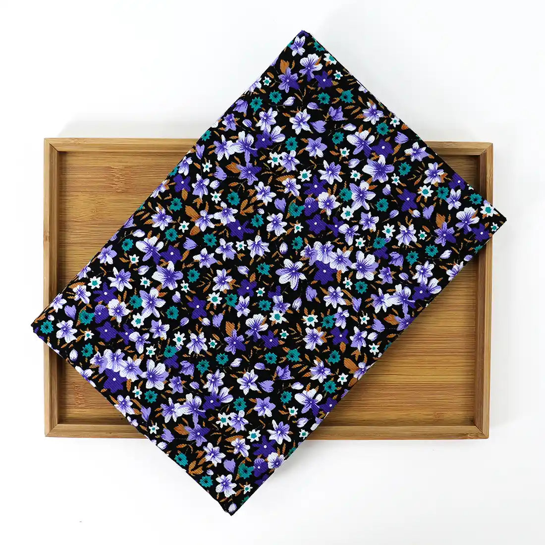 Un Longan Craft France Velours côtelé coton imprimé lys au mètre, présentant un motif floral bleu, violet et brun, est présenté en diagonale sur un plateau rectangulaire en bois sur fond blanc.