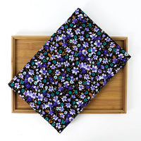 Un Longan Craft France Velours côtelé coton imprimé lys au mètre, présentant un motif floral bleu, violet et brun, est présenté en diagonale sur un plateau rectangulaire en bois sur fond blanc.