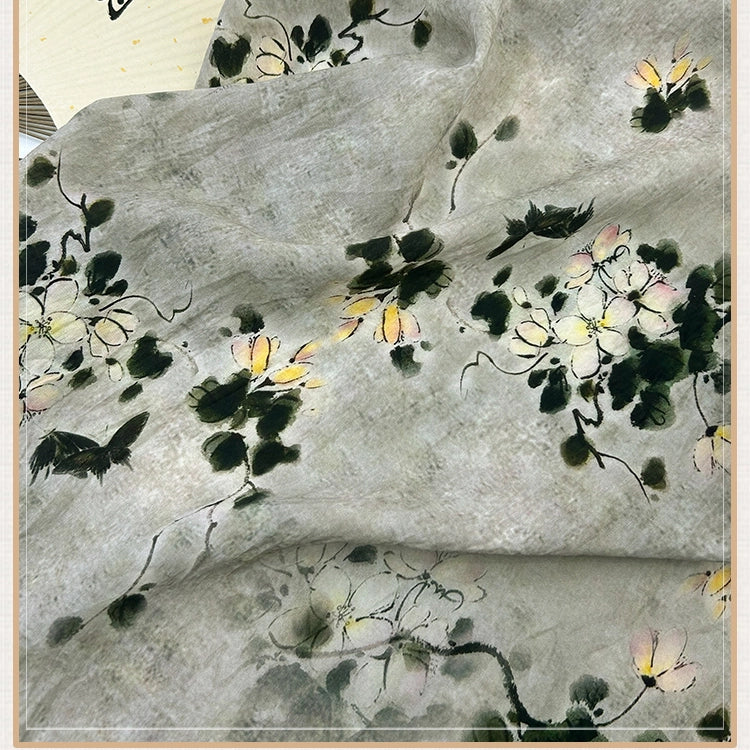 Tissu en lin lyocell imprimé au motif floral style chinoiserie de Longan Craft France, avec branches noires, feuilles vertes et fleurs blanc-jaune sur fond gris. Vendu au mètre.
