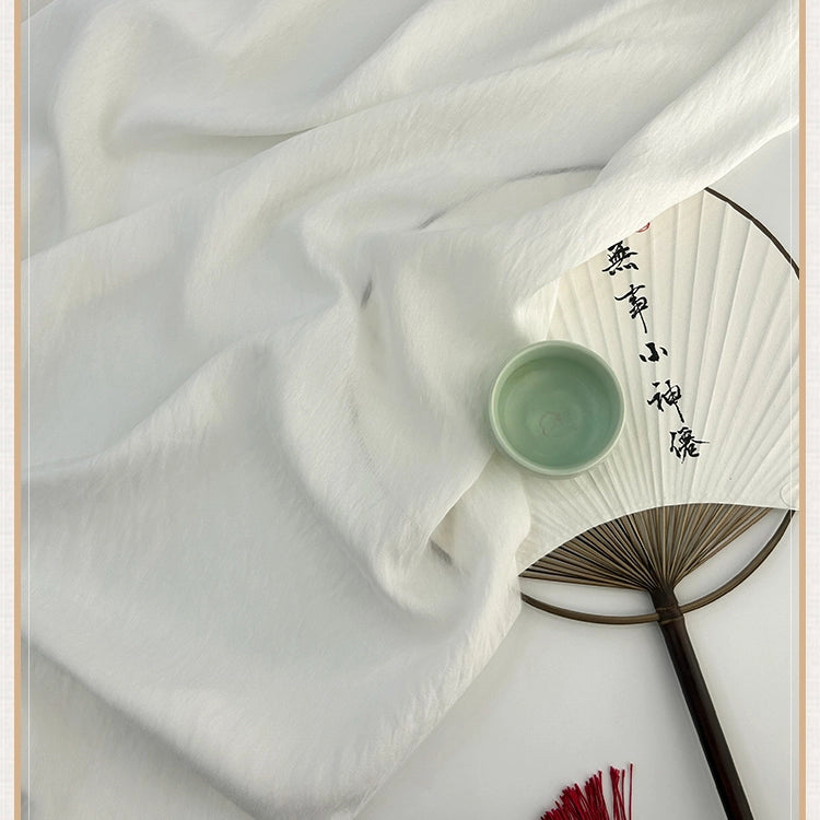 Un tissu lyocell en lin de style chinoiserie vintage de Longan Craft France est drapé à côté d'un éventail en papier à caractères chinois et surmonté d'un petit bol en céramique verte, tandis qu'un pompon rouge apparaît au bas de l'étagère.