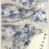 Gros plan sur le tissu chinoiserie vintage en lin-lyocell de Longan Craft France au mètre, qui présente un motif de bambou et de feuilles bleu clair, semi-transparent, avec une calligraphie partielle en noir sur le bord.
