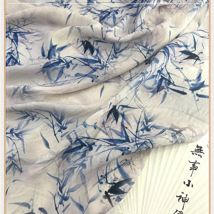 Gros plan sur le tissu chinoiserie vintage en lin-lyocell de Longan Craft France au mètre, qui présente un motif de bambou et de feuilles bleu clair, semi-transparent, avec une calligraphie partielle en noir sur le bord.