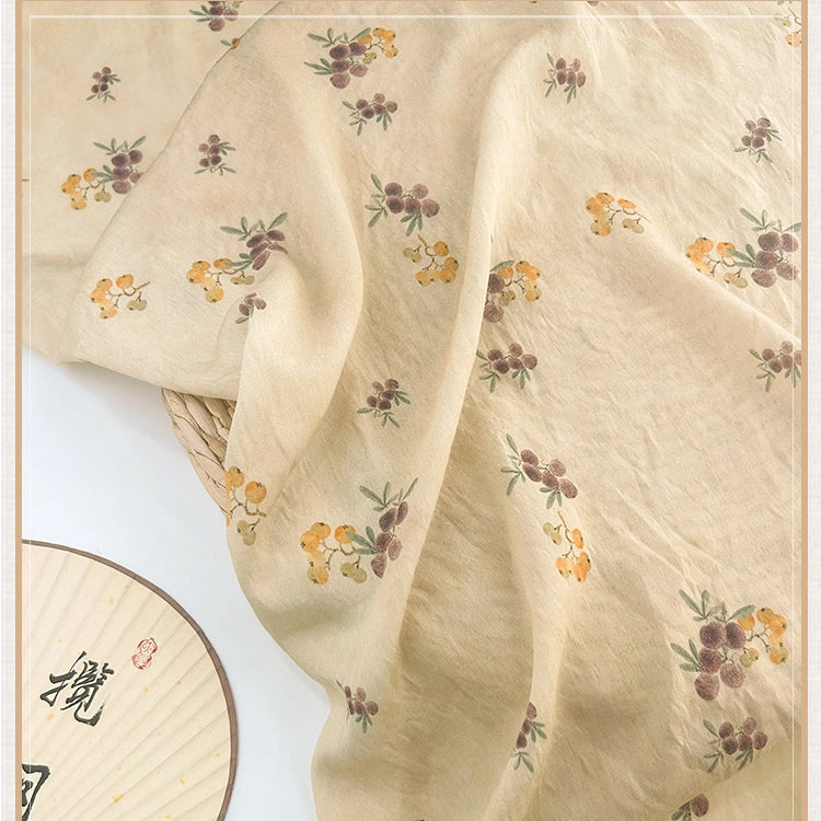 Le Tissu en lin imprimé vintage style chinoiserie au mètre de Longan Craft France présente un tissu beige clair en lin lyocell, orné de petites fleurs jaunes et violettes, avec un éventail rond à motifs chinois visible dans le coin inférieur gauche.