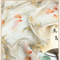 Un tissu doux en lin et lyocell de Longan Craft France, avec des motifs de chinoiseries de poissons rouges et orange et des fleurs subtiles, est drapé pour couvrir partiellement un éventail à main avec des écritures asiatiques. Tissu en lin imprimé vintage au mètre.