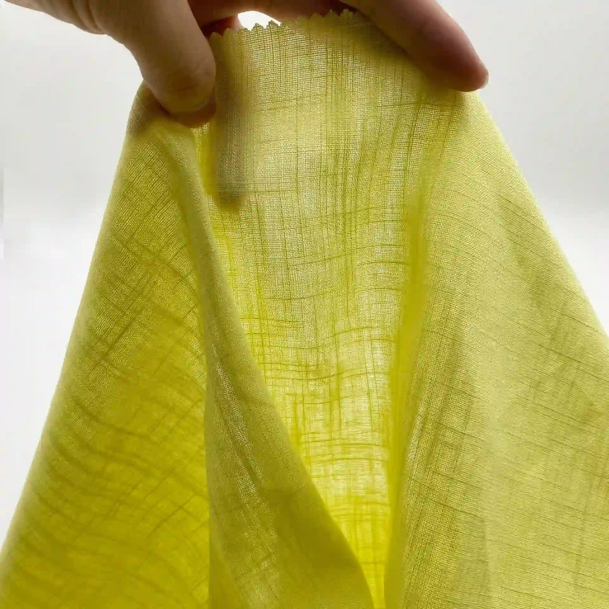 Une main tient un Tissu lin viscose au mètre semi-transparent de Longan Craft France sur un fond blanc, mettant en valeur la viscose cellulosique légère et multicolore idéale pour les tenues d'été.