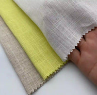 Une main tient trois échantillons superposés de Tissu lin viscose au mètre de Longan Craft France en beige, jaune et blanc. Les bords en lin visiblement tissés, coupés à la cisaille, montrent cette matière viscose idéale pour l'été.
