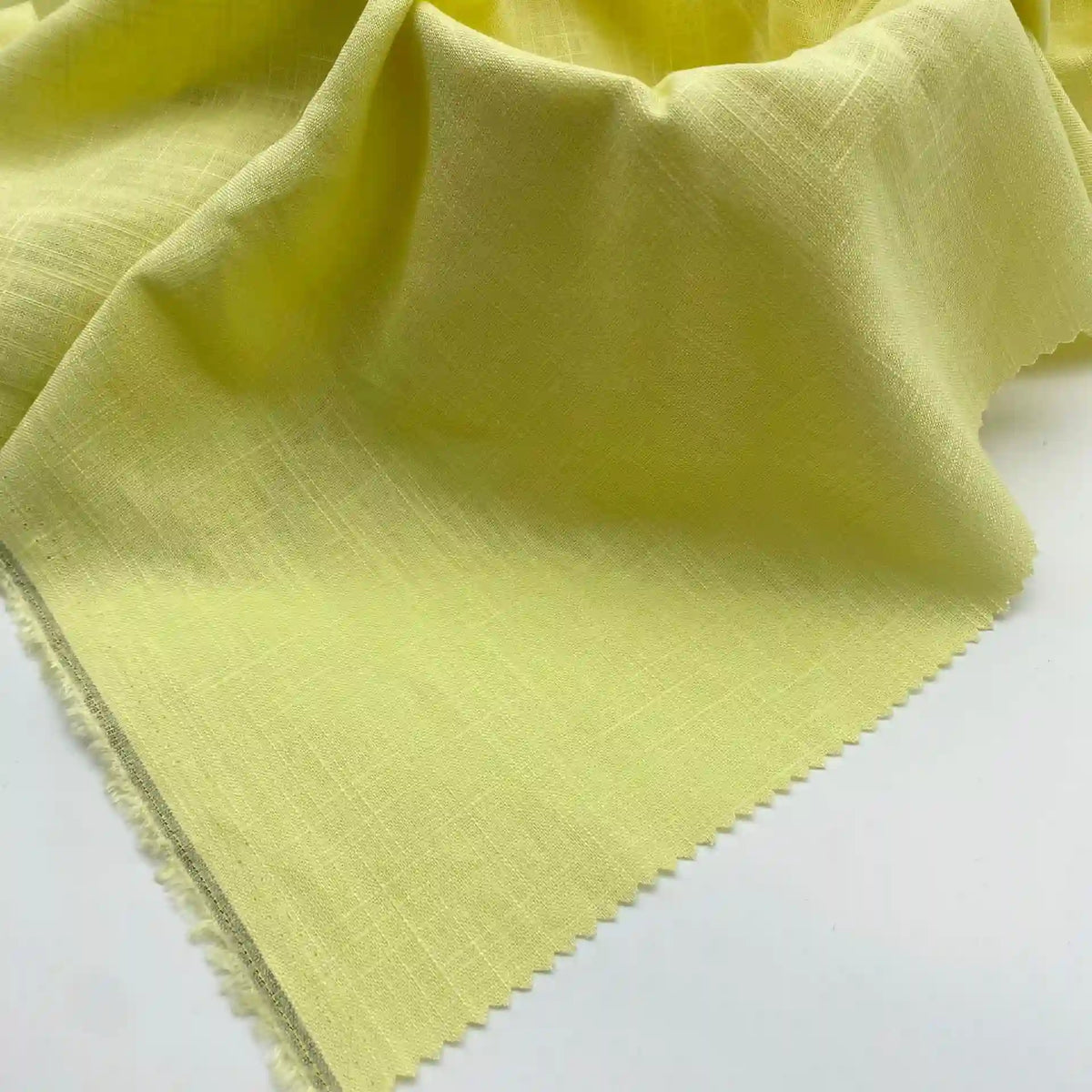Gros plan sur le tissu lin viscose au mètre Longan Craft France, matière viscose cellulosique multicolore idéale pour l'été, en jaune pâle avec texture visible, drapé sur une surface blanche et une bordure découpée aux ciseaux cranteurs.