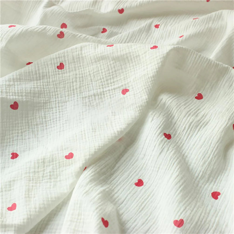 Gros plan sur le Tissu double regard petit cœur au mètre de Longan Craft France, un crêpe 100 % coton à la texture froissée, avec des motifs de cœurs rouges régulièrement espacés.