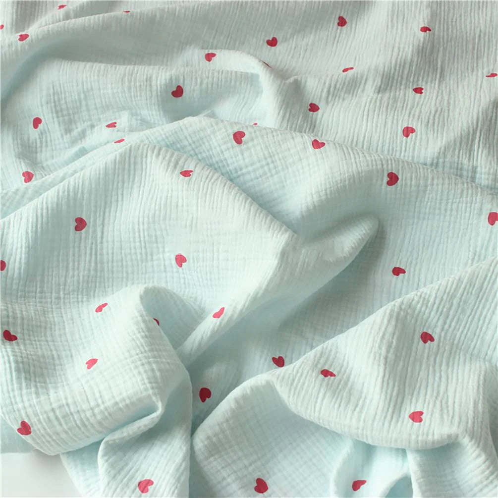 Tissu double gaze petit cœur au mètre de Longan Craft France : crêpe doux 100% coton avec une texture quadrillée bleu clair et des motifs de cœurs rouges éparpillés, parfait pour des plis doux et un look délicat et texturé.