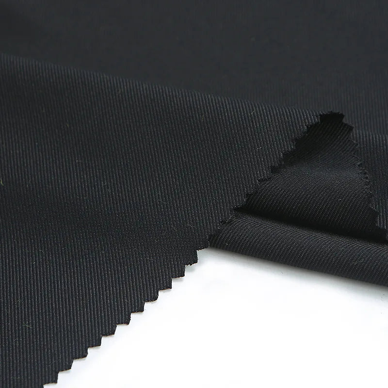 Gros plan sur le tissu gabardine de Longan Craft France, caractérisé par un tissage diagonal subtil et des bords coupés en zigzag, présenté sur une surface blanche. Ce textile mat de haute qualité est idéal pour les vestes et se vend au mètre.