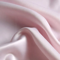 Gros plan sur le Tissu satin mat uni de Longan Craft France, un tissu de satin de polyester rose pâle aux plis souples et au drapé doux, idéal pour les vêtements élégants et disponible au mètre.